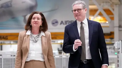 Reuters Eluned Morgan, una mujer de cabello oscuro con traje marrón y camisa blanca, camina con Sir Keir Starmer, un hombre con traje azul marino, camisa blanca y corbata gris.
