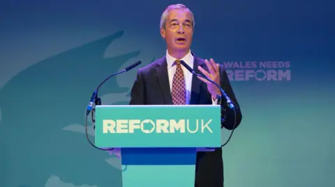 Getty Images Nigel Farage, un hombre con traje azul marino, sube a un podio con 