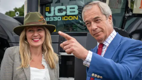 Getty Images Laura Anne Jones, una mujer de largo cabello rubio, que viste un sombrero verde y una chaqueta de tweed, sonríe mientras está junto a Nigel Farage, un hombre con traje azul, camisa blanca a cuadros y corbata roja, que señala a alguien de la cámara.