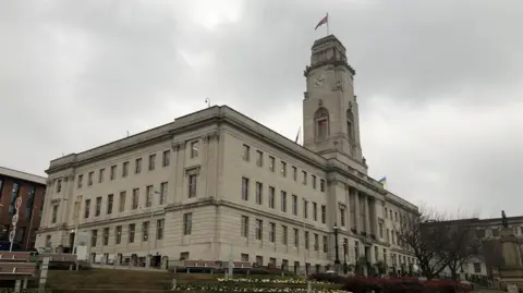 Ayuntamiento de Barnsley, un gran edificio rectangular de piedra en Barnsley. Tiene una gran torre de reloj rematada por una bandera sindical.