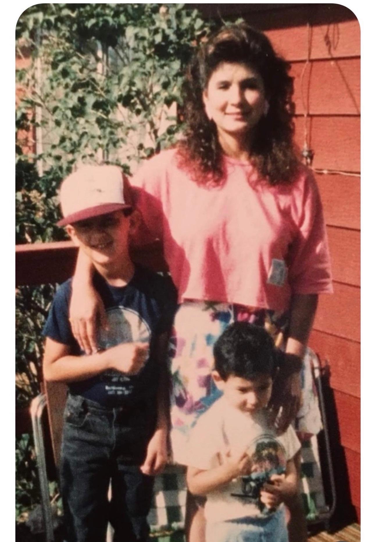 Una película antigua de la líder de la mayoría demócrata de la Cámara de Representantes, Mónica Durán, con sus dos hijos pequeños parados frente a ella. Su brazo rodea a un niño mayor que lleva una gorra de béisbol. Un niño más joven sostiene un juguete.