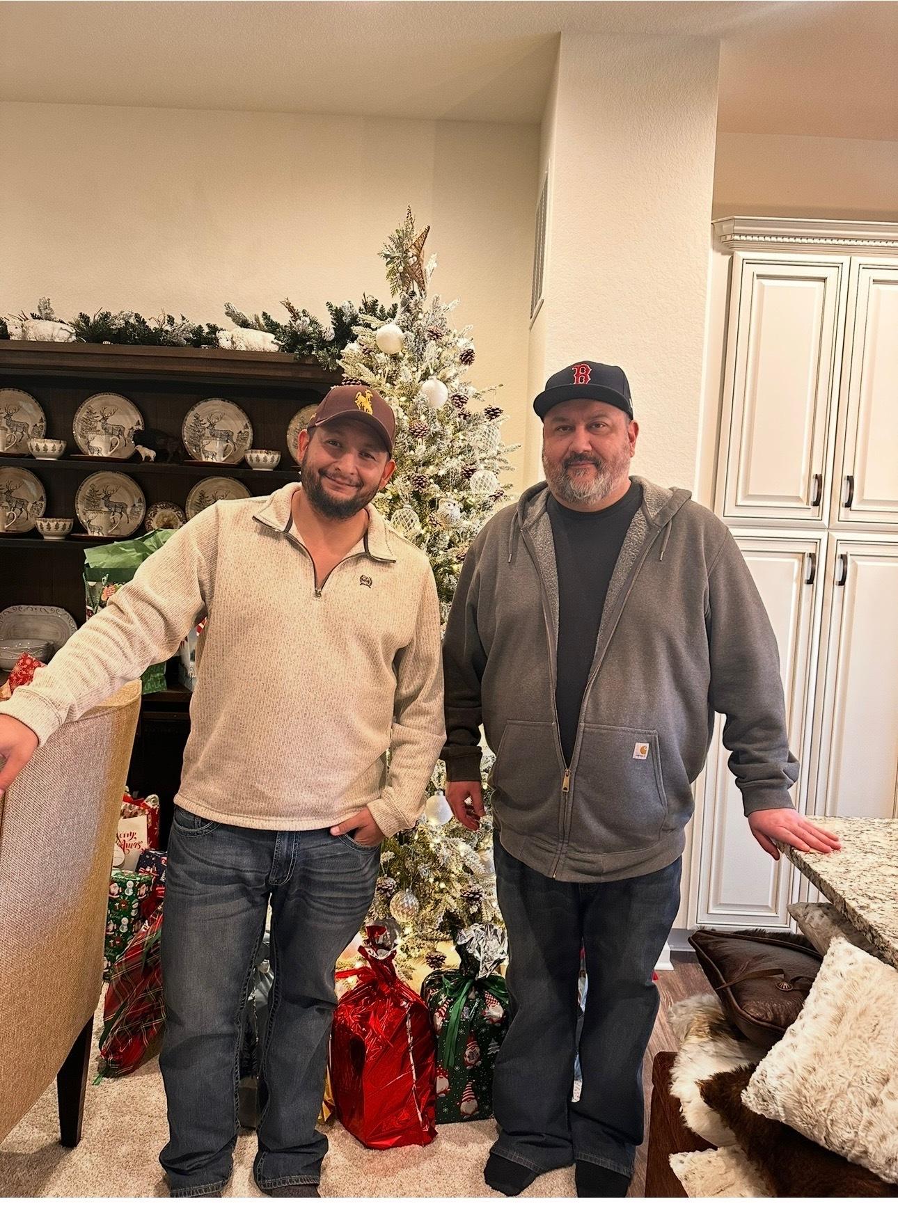 Patrick Ellis (izquierda) y David Duran (derecha) están en la sala de estar frente al árbol de Navidad.
