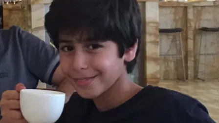 Mohammed Algasim es representado como un niño bebiendo de una taza de café con leche. Está sonriendo a la cámara y lleva un suéter Timberland negro.